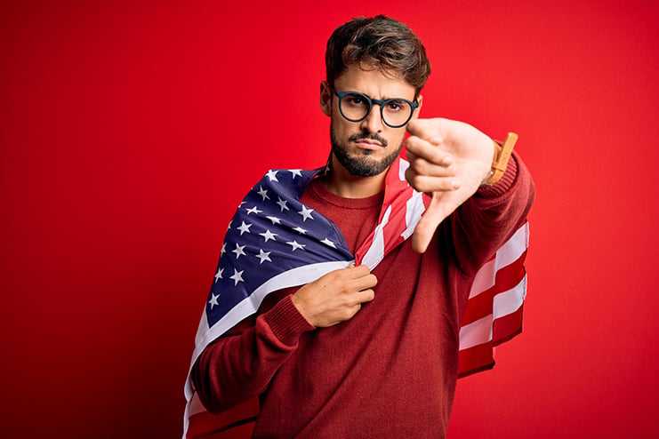Young man wearing glasses and United States of America flag over isolated red background with angry face, negative sign showing dislike with thumbs down, rejection concept Red Herrings of the Official Neocon History of the U.S.