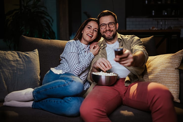 Happy couple watching tv and eating popcorn on sofa at night Replace Awful Late-Night Shows with Arts TV