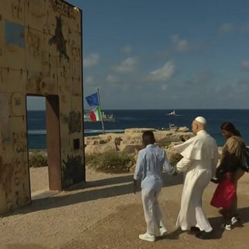 POPE_Lampedusa Caption: Pope Leo XIV walks hand-in-hand with African migrants through the "Gateway to Europe" monument on July 4, 2026, on the Italian island of Lampedusa. (Vatican News / Vatican Dicastery for Communication)